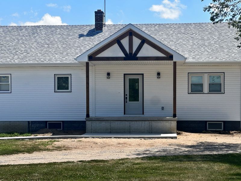 Covered front entry with a cedar timber-accent gable on a white-sided home with a gray shingle roof