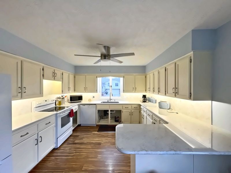 Remodeled kitchen with white cabinets, white quartz countertops, a hexagon tile backsplash and wood floors