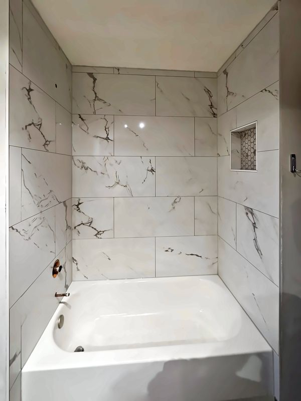 Bathtub with a floor-to-ceiling marble-look tile surround and a built-in shower niche